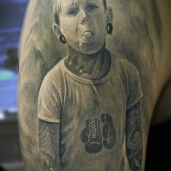 Мальчик с татуировками на теле и тоннелями в ушах показывает язык