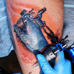 Рука татуировщика с тату машинкой